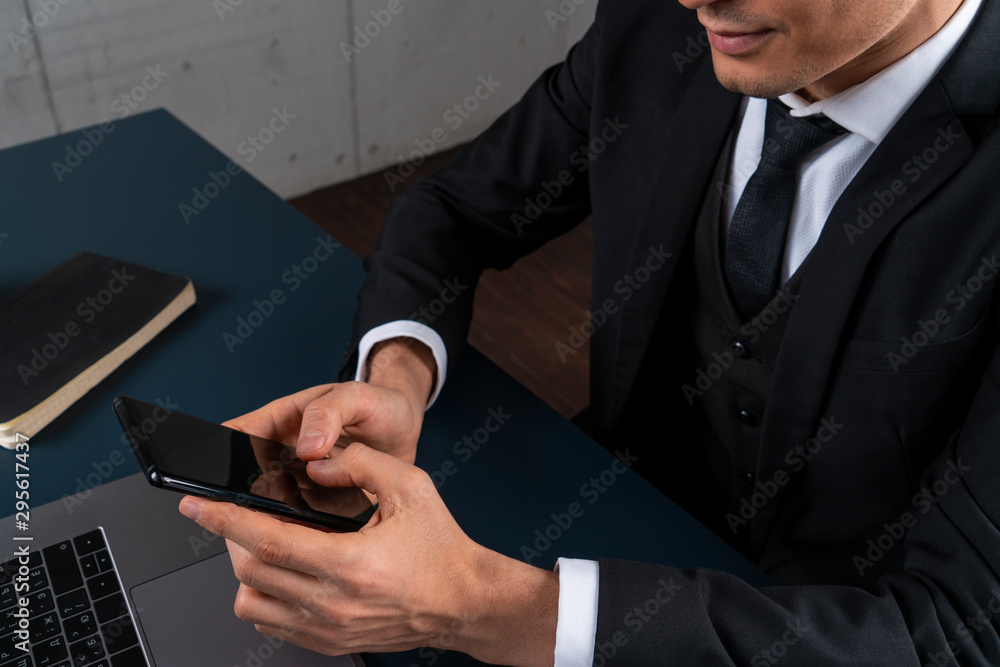 Top view of young unrecognizable businessman using smartphone at loft office table with copybook and laptop. Concept of business communication Top view of young unrecognizable businessman using smartphone at loft office table with copybook and laptop. Concept of business communication