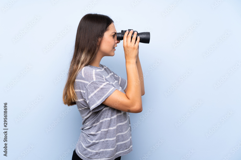 Young brunette woman over isolated blue background with black binoculars Young brunette woman over isolated blue background with black binoculars