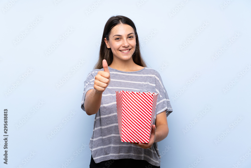 Young brunette woman over isolated blue background holding a bowl of popcorns Young brunette woman over isolated blue background holding a bowl of popcorns