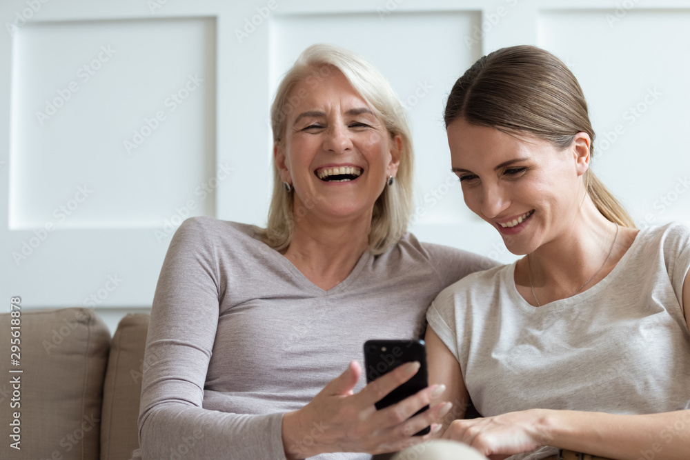 Mother and adult daughter watching funny videos on smartphone laughing Mother and adult daughter watching funny videos on smartphone laughing