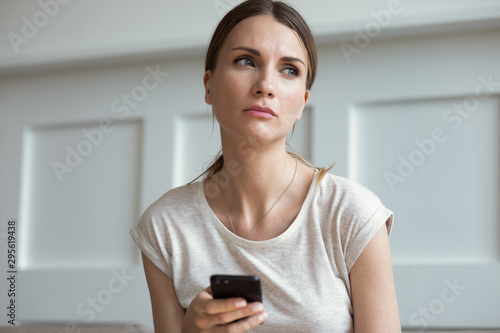 Fotografia, Obraz Sad woman holding smartphone waiting call from boyfriend feels jealousy