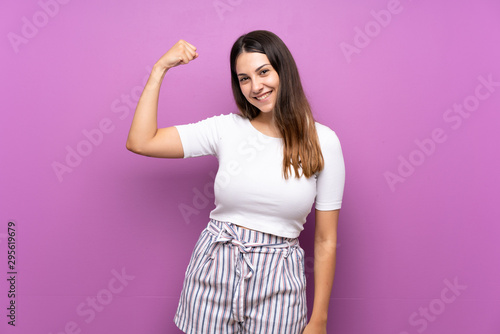 Young woman over isolated purple background doing strong gesture © luismolinero