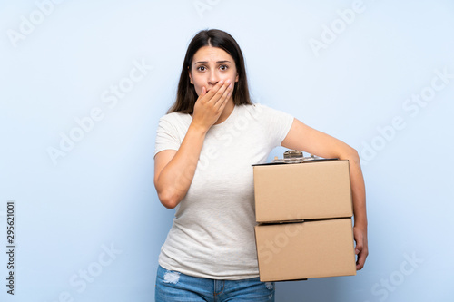Young delivery woman over blue brick wall with surprise facial expression