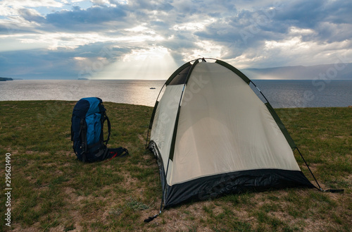 Empty tent with backpack of travelers on green terrain in bright sunset light