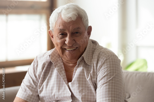 Elderly man seated on couch smiles looking at camera