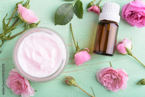 Homemade creame and essential oil with roses on wooden background.