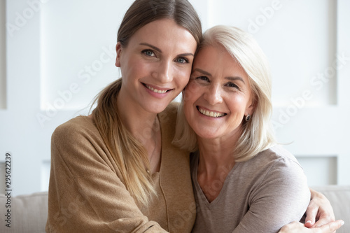 Attractive aged mother and adult daughter hugging looking at camera photo