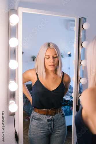 Girl trying clothes looking in mirror cheerful and happy. Cute beautiful caucasian gil with hipster white dyed hair. Fashion and blogger lifestyle. Choose the perfect outfit for start the day. photo