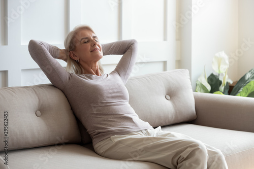 Older 50s female resting seated on couch with closed eyes