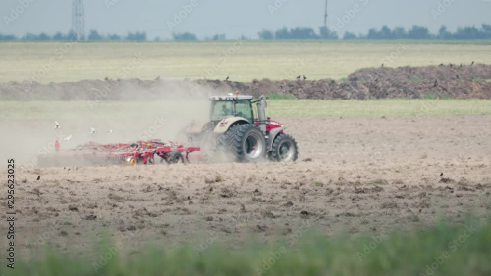 Tractor processing of the field in the spring, soil preparation by mechanical mixing of different types and layers in the early spring period of agricultural work on the farm. Side view Tractor processing of the field in the spring, soil preparation by mechanical mixing of different types and layers in the early spring period of agricultural work on the farm. Side view