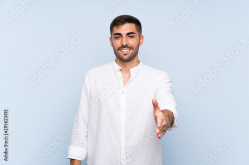 Handsome man with beard over isolated blue background shaking hands for closing a good deal