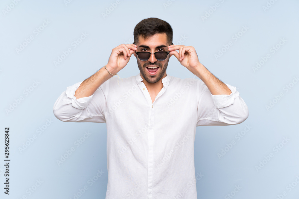 Handsome man with beard over isolated blue background with glasses and surprised Handsome man with beard over isolated blue background with glasses and surprised