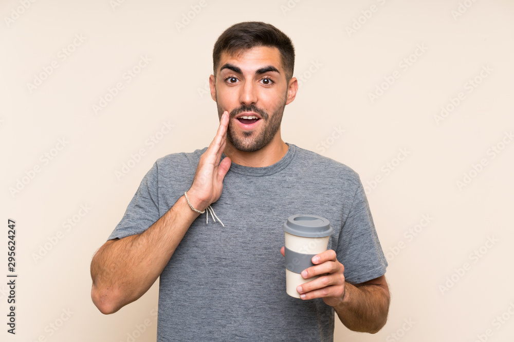 Handsome man with beard holding a take away coffee over isolated background with surprise and shocked facial expression Handsome man with beard holding a take away coffee over isolated background with surprise and shocked facial expression
