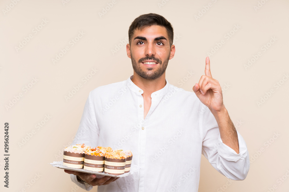 Handsome man holding muffin cake over isolated background intending to realizes the solution while lifting a finger up Handsome man holding muffin cake over isolated background intending to realizes the solution while lifting a finger up