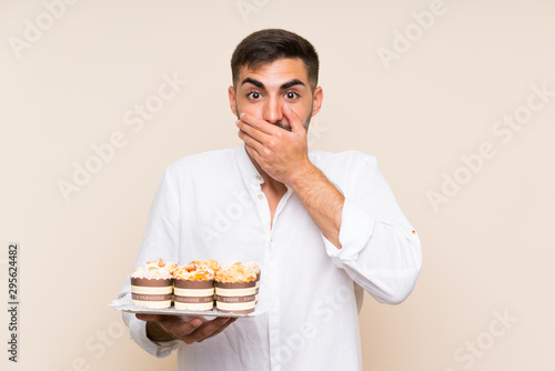 Handsome man holding muffin cake over isolated background with surprise facial expression