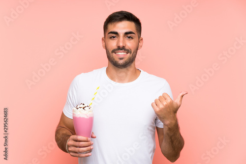 Young man with strawberry milkshake over isolated pink background pointing to the side to present a product