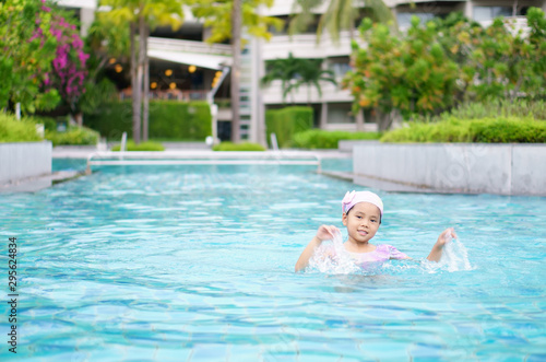 Asian child cute swim or kid girl wear swimming suit and cap on swimming pool and play enjoy or smiling with happy fun in water park for learning or splash and healthy with exercise on summer holiday © kornnphoto