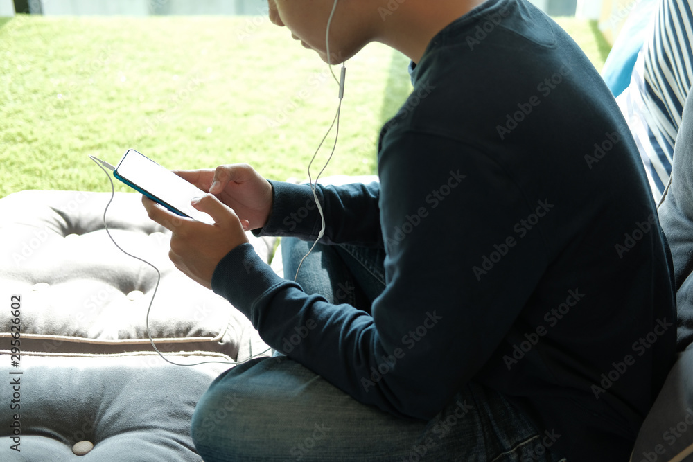 asian teenager man listening to music from smart mobile phone while sitting on floor at home