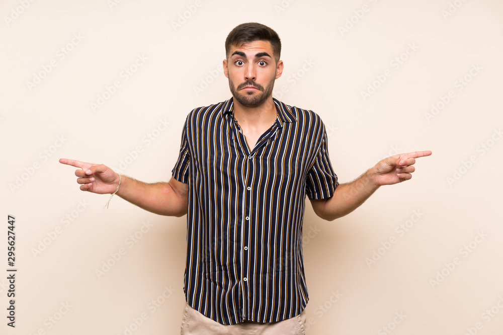 Handsome man with beard over isolated background pointing to the laterals having doubts Handsome man with beard over isolated background pointing to the laterals having doubts