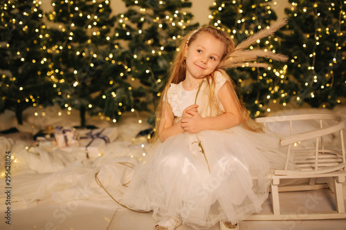 Little girl sitting on sleigh at home in front o Christmas trees. Winter holiday