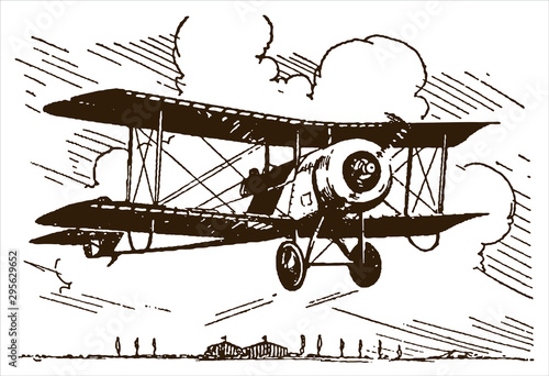 Historical single-seat rotary-engined racing biplane flying over trees and hangars near an airfield