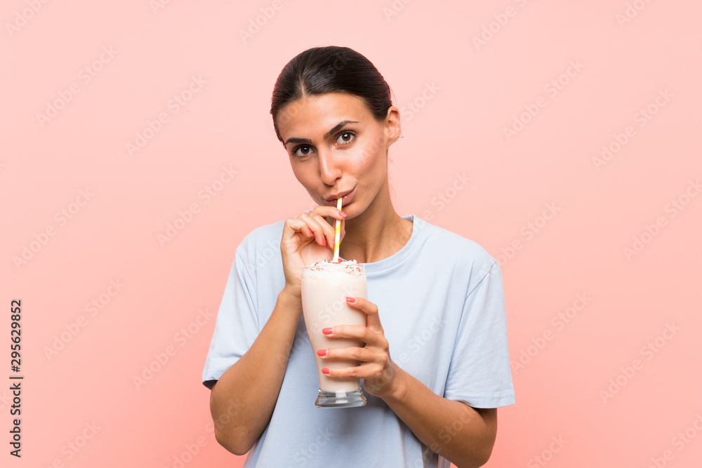 Young woman with strawberry milkshake over isolated pink background Young woman with strawberry milkshake over isolated pink background