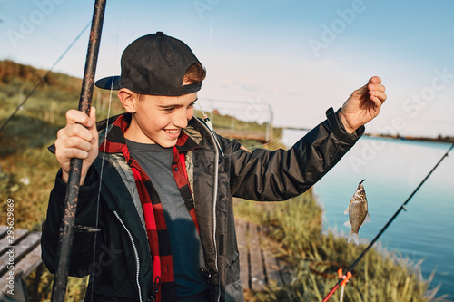 Teen caucasian boy catch first fish. He smiles, happy, look, show fish.