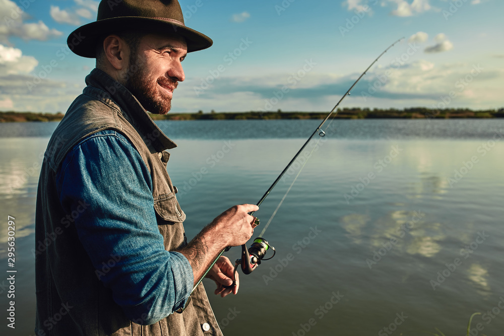 Caucasian adult bearded men stand near lake and hold fishing rod. Here he with his son, he shows how hold fishing rod correctly. Caucasian adult bearded men stand near lake and hold fishing rod. Here he with his son, he shows how hold fishing rod correctly.