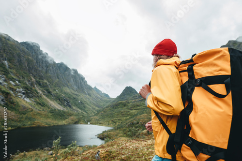 Tourist with backpack standing in front of the mountain massif while journey by scandinavian. Male traveler wearing yellow jacket explore national park and hiking outdoor landscape