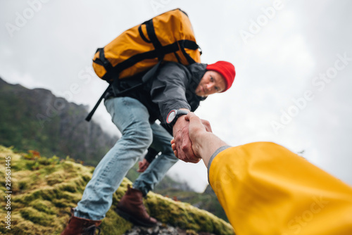 Group of two active tourist with backpack climb to rock helping each other. Brave traveler hold hand his friend for helping climb to mountain lifestyle outdoor journey
