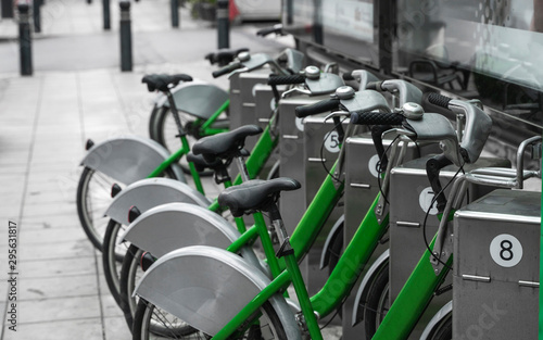 Street transportation green hybrid rent bicycles with electronic form of payment for traveling around the city stand in row on rental network parking lot waiting for cyclists to make bike trip.