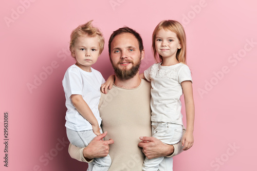 handsome father carrying his little daughter and son on pink background, happy fatherhood, lifestyle, close up portrait