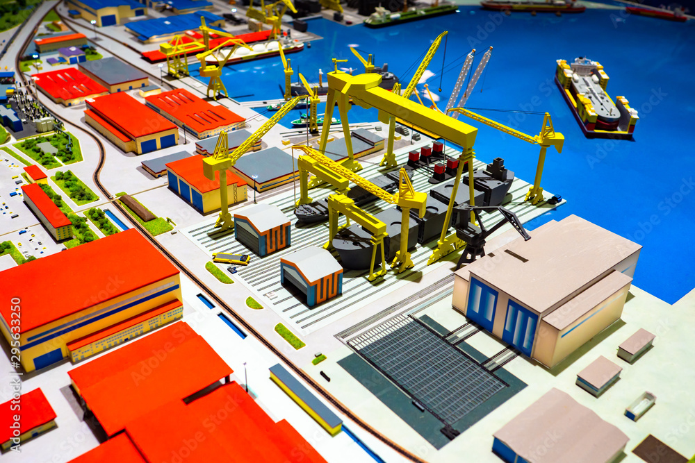 Layout commercial sea port. Yellow cranes and gantry cranes. Cranes for loading and unloading. Warehouses for storage of goods. Hangars. Container ship on the water.
