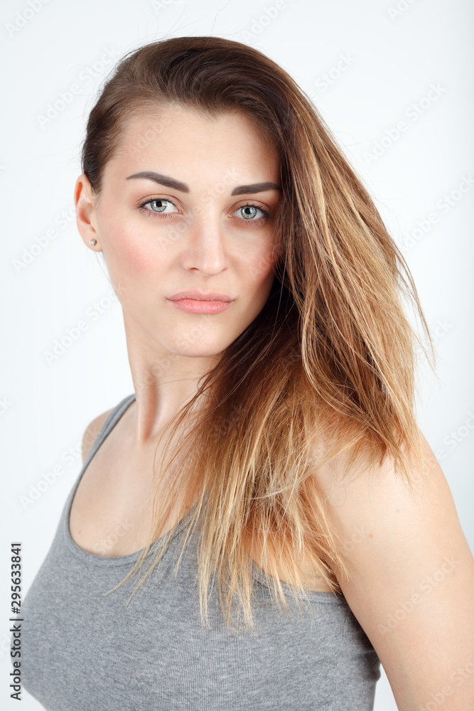 Young beautiful girl in a gray t-shirt on a white background looks at the camera and smiles Young beautiful girl in a gray t-shirt on a white background looks at the camera and smiles