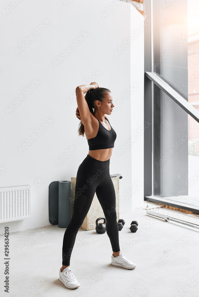 Athletic female doing exercises standing at gym. Dressed in black clothes. Background window Athletic female doing exercises standing at gym. Dressed in black clothes. Background window