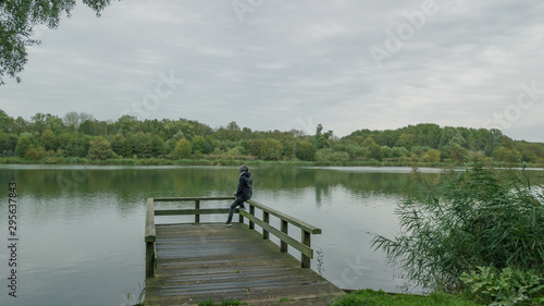 Autumn mood at the lake. Woman with warm clothes on a dock at a lake.Cloudy sky.