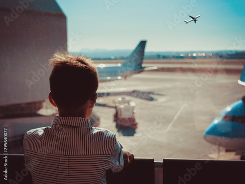 European boy in striped shirt looking through airport window on plane’s taking off. He waiting for his flight. Back view.