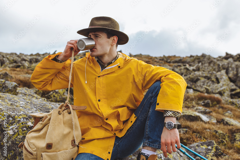 Fototapeta premium young stylish traveller enjoying drinking hor tea while sitting on the hill. close up photo
