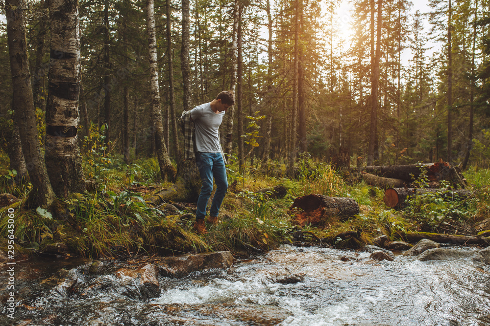 young man taking off clothes while standing on the bank of the river, he is going to swim, full length photo. copy space