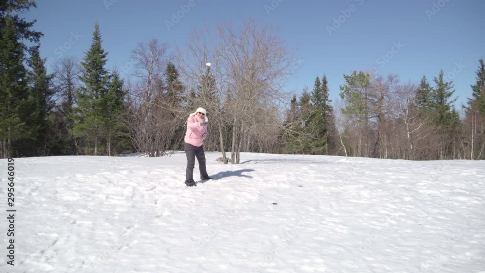 Grandmother has fun in the winter on the street in children's games. Funny throwing snowballs at the camera.
