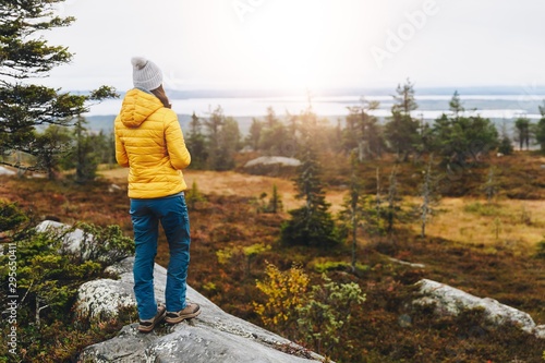 Fotografie, Obraz Woman traveler in yellow jacket from back hike in autumn forest in Finland Lapland