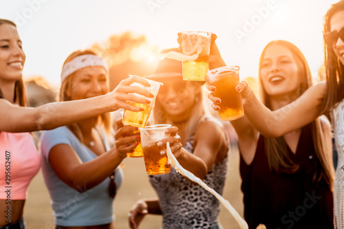 Female friends cheering with beer at music festival. splash