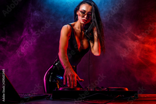 Young sexy woman dj playing music. Headphones and dj mixer on table. Smoke on background