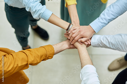 Friends keep hands together in sign of friendship and unity, shot from above, background of light coloured floor, people peace concept © alfa27