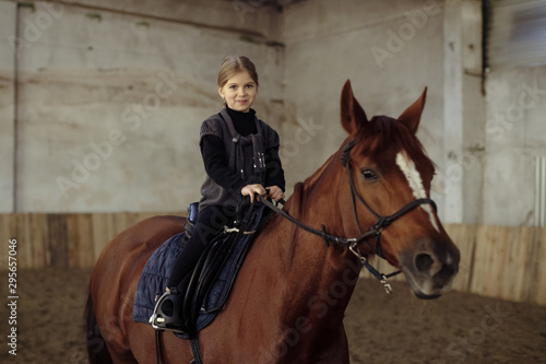 a little girl sits astride a horse in the stable building . © Delete