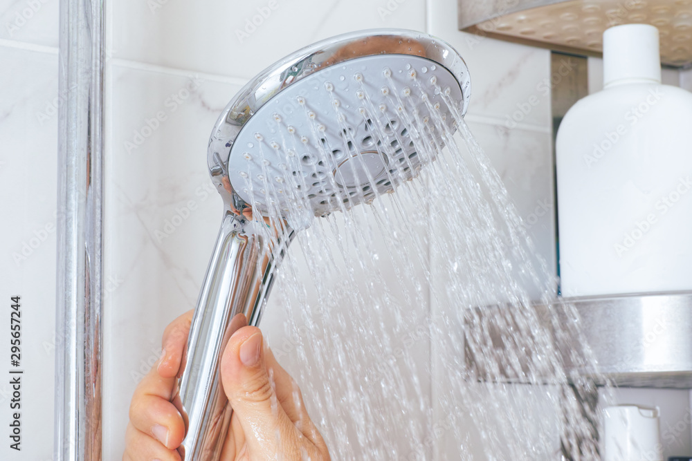 Woman hand using shower head in bathroom. - obrazy, fototapety, plakaty 