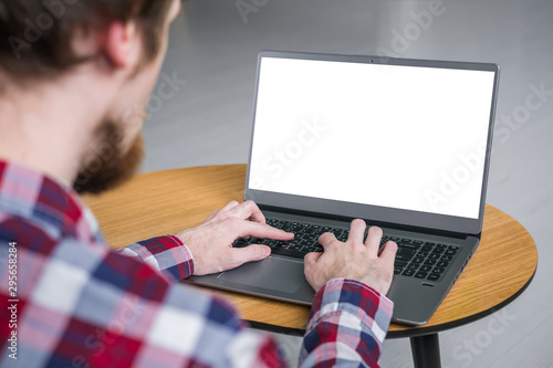 Mockup image: man typing on laptop computer keyboard with white blank screen on wooden table in home or cafe. Mock up, copyspace, freelance workspace, template, entertainment and technology concept