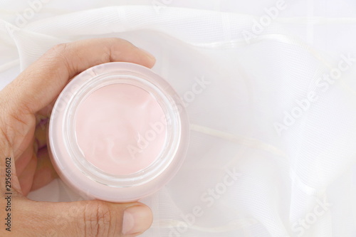 Top view of close up woman hand holding pink cream jar on white fabric background, have copy space