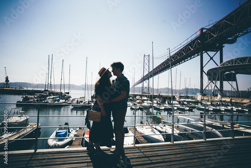 Romantic couplehugging in front of the bridge called April 25 in Lisbon and yachts port in Portugal at sunny summer day. photo