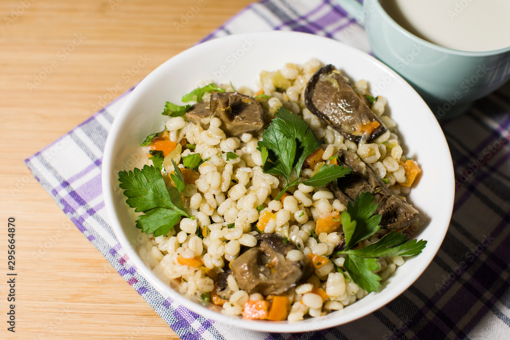 Vegetarian crumbly pearl barley porridge with mushrooms vegetables and herbs in a white plate Vegetarian crumbly pearl barley porridge with mushrooms vegetables and herbs in a white plate